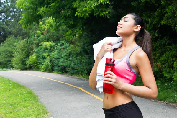 Молодая женщина отдыхает с полотенцем и бутылкой воды после бега — стоковое фото