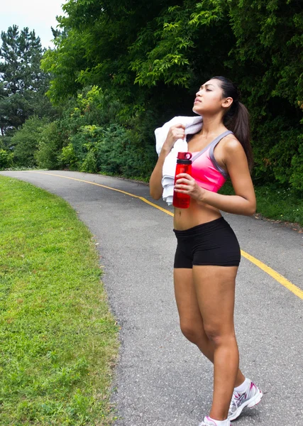 Jonge vrouw met handdoek en water fles rusten na het lopen — Stockfoto
