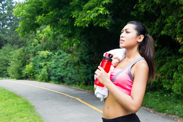 Jonge vrouw met handdoek en water fles rusten na het lopen — Stockfoto