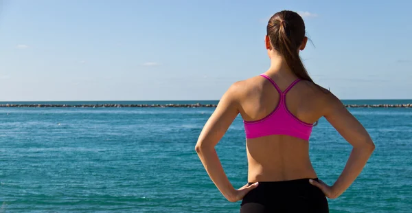 Mujer en sujetador deportivo mirando al océano — Foto de Stock