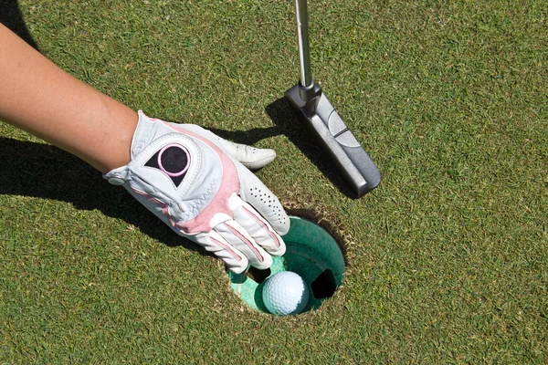 Vrouw gehandschoende hand, putter en golf bal in de cup — Stockfoto