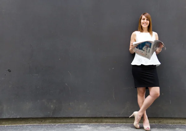 Ділова жінка читає газету, спираючись на стіну — стокове фото