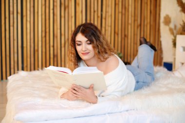 İçeride kitap okuyan, kanepede yatan güzel genç bir kadın.