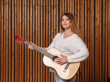 Güzel genç bir kadın klasik gitar çalar, tahta bir duvarın arkasında.