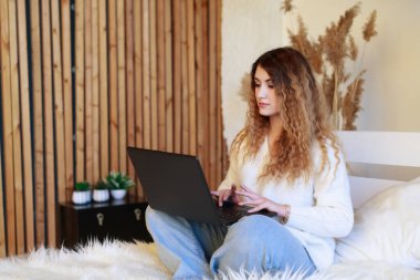 Genç serbest çalışan bir kadın evinde kanepede dizüstü bilgisayar kullanıyor ve uzaktan çalışıyor..