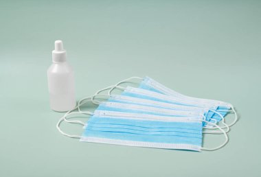 Alkol jeli el dezenfektanı ve mavi arka planda fotokopi alanı olan tek kullanımlık hijyenik maske. Bir şişe el dezenfektanı, antimikrobik sıvı sprey, mikrop önleme veya antibakteriyel hijyen, fotokopi alanı.