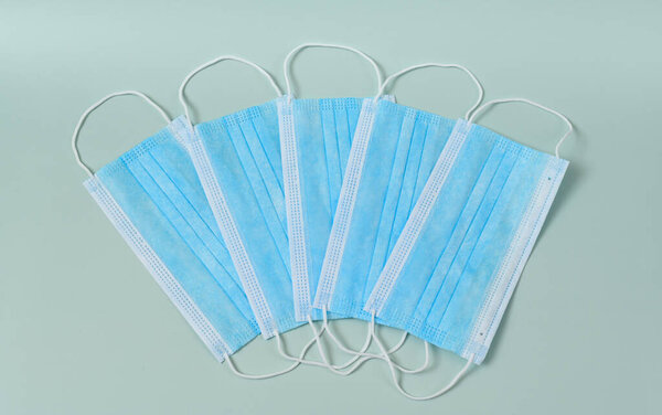 Several medical protective masks lying in a row on a light blue background