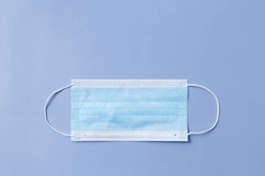 One medical face mask lies horizontally on a blue background.