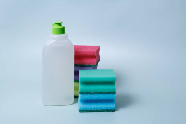 Sponges for washing dishes of different colors and a bottle of liquid detergent on a blue background.