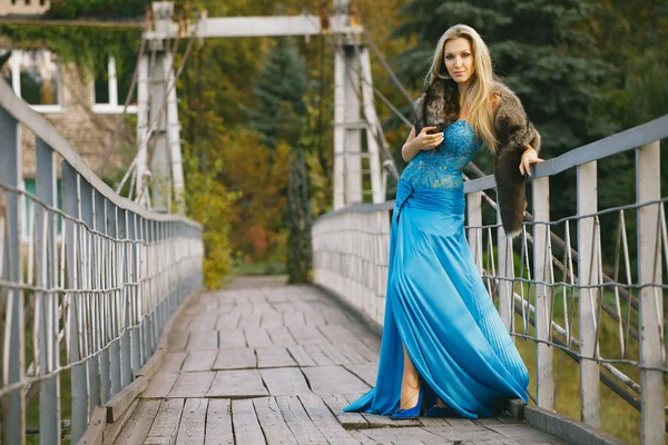 Vacker blond flicka står på bron i parken. — Stockfoto