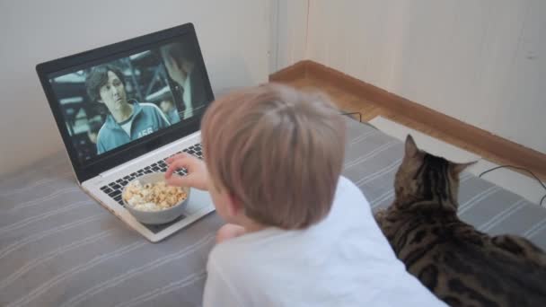 Fryazino,モスクワ地方,ロシア- 2021年10月24日:ラップトップ画面上のNetflixシリーズ.シリーズイカゲーム。子供はテレビシリーズを見てポップコーンを食べる。猫は近くの家の環境にいます — ストック動画