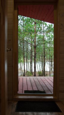 Güzel doğa, ahşap bir evin açık kapısından görülebilir. Orman ve gölet, eğlence ve çevre dostluğu