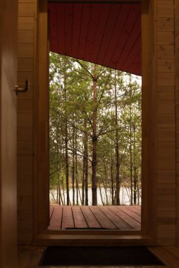Güzel doğa, ahşap bir evin açık kapısından görülebilir. Orman ve gölet, eğlence ve çevre dostluğu