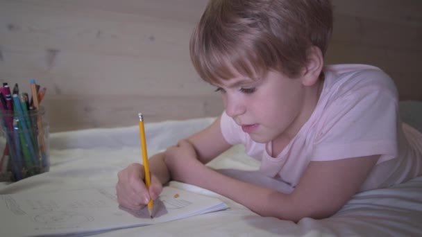 Дитина малює, лежачи в ліжку. Шкільна дівчинка вдома. Домашнє завдання, хобі — стокове відео