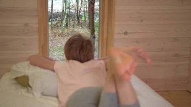 子供はベッドの上に寝そべって窓の外を見る。裸の足を閉じる。健康な足、平らな足の兆候はありません. — ストック動画