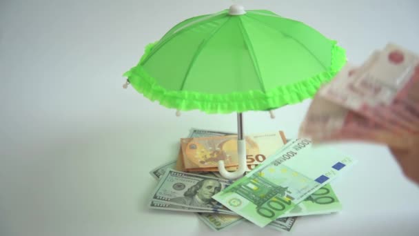 As mãos fecham as contas. Diversificação das finanças. Euros, dólares e rublos. Dividindo suas economias em diferentes moedas. As mãos colocam as contas debaixo do guarda-chuva. O conceito de — Vídeo de Stock