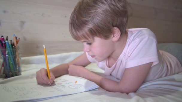 Das Kind zeichnet, während es im Bett liegt. Schulmädchen auf dem Heimweg. Hausaufgaben, Hobbys — Stockvideo