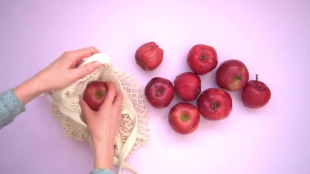 Yukarıdan yakından bak. Büyük kırmızı elmaları ağ torbasına koyan kadın elleri. Çevre dostu ürünler kavramı. Elma alıp satmak.. — Stok video