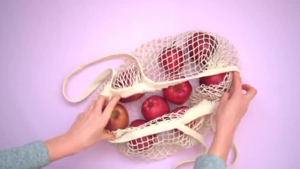 Kvinnors händer lägger äpplen ur en påse. Röda saftiga äpplen i en miljövänlig nätpåse. — Stockvideo