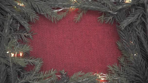 Background for Christmas cards and greetings. Red burlap in a frame of Christmas tree branches and garlands. New Year and Christmas. — Stock Video