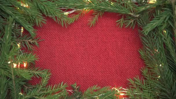 Pozadí pro vánoční přání a pozdravy. Červený důlek v rámu větví a věnců vánočního stromku. Nový rok a Vánoce. — Stock video