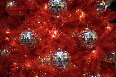 Alışılmadık kırmızı bir Noel ağacı. Noel ağacı disko toplarıyla süslenmiş. Tarz kavramı. Trend. Cesaret ve tuhaflık.