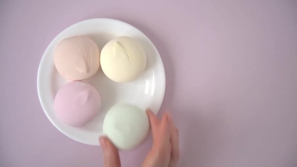 Una mano de mujer toma dulces de un plato blanco. Vista desde arriba. Colores pastel suaves — Vídeos de Stock