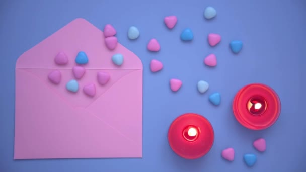 Ιστορικό για την Ημέρα του Αγίου Βαλεντίνου. Θέα από ψηλά. Ροζ φάκελο και πολύχρωμες καρδιές. Τα κόκκινα κεριά καίγονται, ένα μπλε φόντο. Η έννοια της δημιουργίας του Αγίου Βαλεντίνου και γράμματα με δηλώσεις αγάπης — Αρχείο Βίντεο