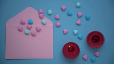 Sevgililer Günü için arka plan. Yukarıdan bak. Pembe zarf ve renkli kalpler. Kırmızı mumlar yanıyor, mavi arka plan. Sonra mumlar sönecek. Sevgililer günü kartı ve mektup yaratma kavramı.
