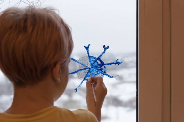 Bir çocuk pencereye bir Noel kar tanesi çizer. Coronavirüs şeklinde bir kar tanesi. Noel ve karantina kavramı. Salgın sırasında yılbaşı konsepti. Evde kal..