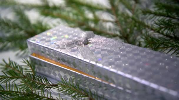 Une boîte argentée scintille entourée de branches d'arbres de Noël. Boîte avec un cadeau de Noël. Une lumière jaune chaude est visible de la boîte. Fond d'écran de Noël. — Video