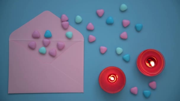 バレンタインデーの背景。上からの眺め。ピンクの封筒とカラフルな心。赤いろうそくは、青い背景が燃えています。愛を宣言してバレンタインや手紙を作るという概念 — ストック動画