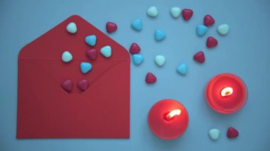 Sevgililer Günü için şık ve rahat bir fotoğraf. Yukarıdan bakıldığında, mavi arkaplanda bir zarf, mumlar ve kalpler vardı. Kalplerin döküldüğü kırmızı bir zarf. Yanan mumlar bir şey yaratır.