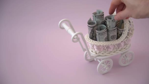 Een vrouwenhand voegt US dollar biljetten toe aan een kinderwagen. Het begrip bijstand en uitkeringen bij de geboorte van een kind. — Stockvideo