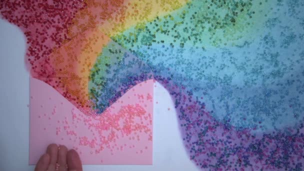 Top view. Womens hands scatter beads or beads on a postcard. A rainbow spilled out of the envelope. All the colors of the rainbow. The concept of good wishes for any holiday. Christmas, Valentines — Vídeo de Stock