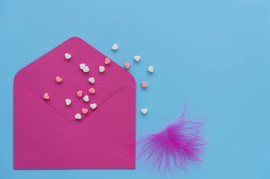 Mavi arka planda pembe bir zarf. Sevgililer Günü kartı için klasik renkler. Açık zarftan küçük renkli kalpler uçar. Sevgililer Günü 'nde tebrik konsepti. Sevgi ve