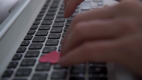 Frauenhände tippen auf einer Laptop-Tastatur. Von oben strömen Konfetti in Herzform. Das Konzept der Glückwünsche zum Valentinstag. Das Konzept eines Liebesbriefes. Valentinstag in — Stockvideo