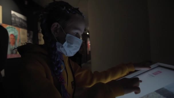 En flicka i medicinsk mask studerar en interaktiv resultattavla. En tonåring på ett museum. Meny i elektronisk form i restaurangen. — Stockvideo