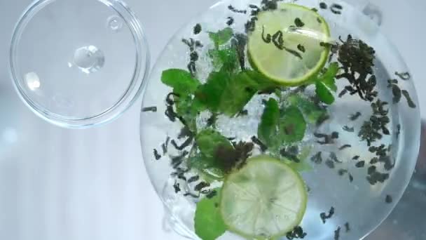 Step by step instruction. Step 2. The process of making green tea. Glass transparent teapot, bottom view. The teapot contains lime, mint leaves and green tea with mango pieces. It remains to pour all — ストック動画