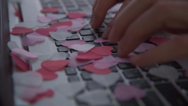 Las manos de mujer escriben en un teclado portátil. Los confeti en forma de corazones comienzan a derramarse desde arriba. El concepto de las felicitaciones por el Día de San Valentín. El concepto de una carta de amor. Valentine en — Vídeos de Stock