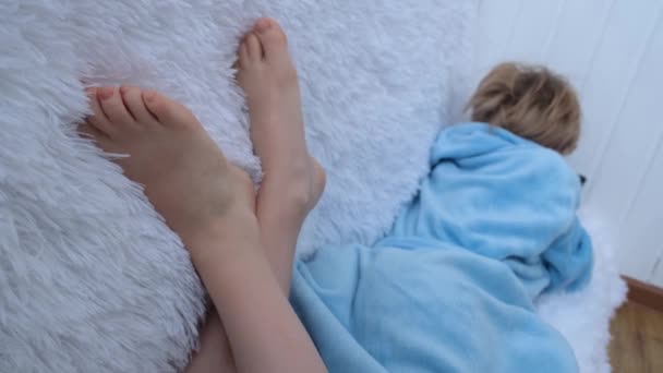 Das Teenager-Mädchen saß gemütlich auf der Couch. Das Kind ist in ein blaues Hausgewand gekleidet. Im Vordergrund stehen nackte Kinderfüße und eine flauschige Decke. Das Kind spielt mit dem Smartphone. Soziales — Stockvideo