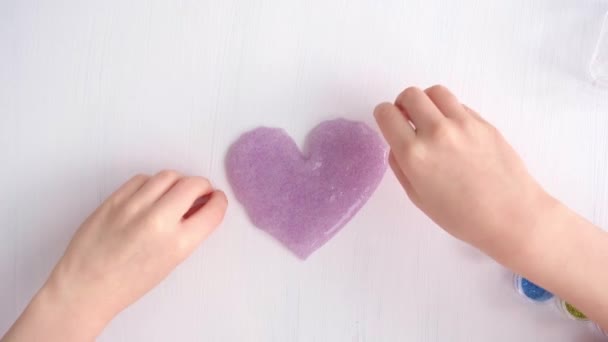 Vista desde arriba. Las manos de los niños hacen una artesanía en forma de corazón. delicado tono lila. Regalo de San Valentín. Trabajos manuales. — Vídeos de Stock