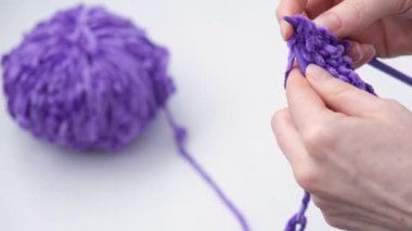 Kadın eli örülmüş. Sonra kadın sonucu düzeltir ve onu topun yanına koyar. Zengin mor renk.