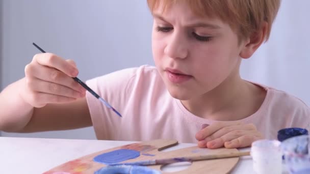 Çocuk ressamların yüzüne yakın çekim. Küçük yetenekli bir adam özenle bir fırçayla resim yapar. Yüz, duyguları ifade eder. Odaklanma ve ciddiyet. Kısa saçlı, güzel bir kızıl çocuk. — Stok video