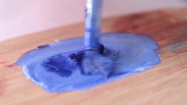 Sanatçı palette boya karıştırır. Fırça beyaz ve mavi boyayı karıştırır. Yakın plan..