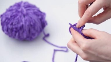 Örgü örme süreci. Kadınların ellerinin yakın çekimi. Örgü örüyorum. Seçici odaklanma. Arka planda bir yün yumağı var. Modaya uygun mor iplik rengi.