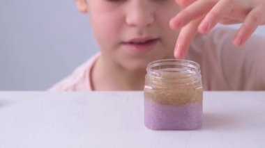 Childs 'ın elleri yakın planda. İlkokul çağındaki bir çocuk sümüğü kavanozdan çıkarır. Farklı renklerde bir leke. Çocuk oyuncağı onun önünde masanın üzerine serer. Dokunuş, duygu.