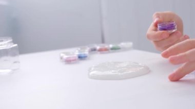 Çocukların elleri, yakın plan. Çocuk balçığa mor parıltılar ekliyor..