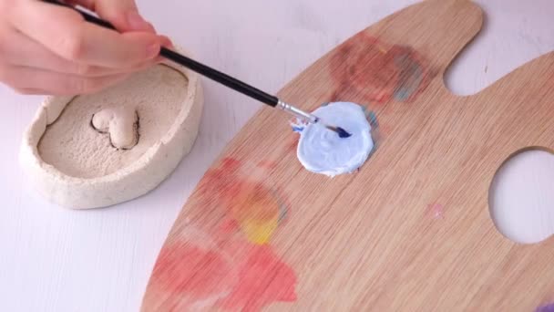 O processo de mistura da tinta para obter a cor azul desejada. Uma mão infantil mistura guache em uma paleta de madeira. Ao lado dele está uma embarcação que precisa ser pintada. Feito à mão, presente. — Vídeo de Stock