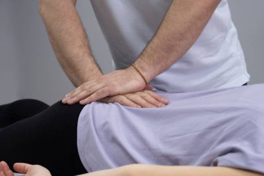 Osteopat kuyruk sokumuyla çalışıyor. Bir manuel terapistin çalışma süreci. Hasta kanepede yatıyor. Doktor kuyruk sokumu bölgesini düzeltiyor.
